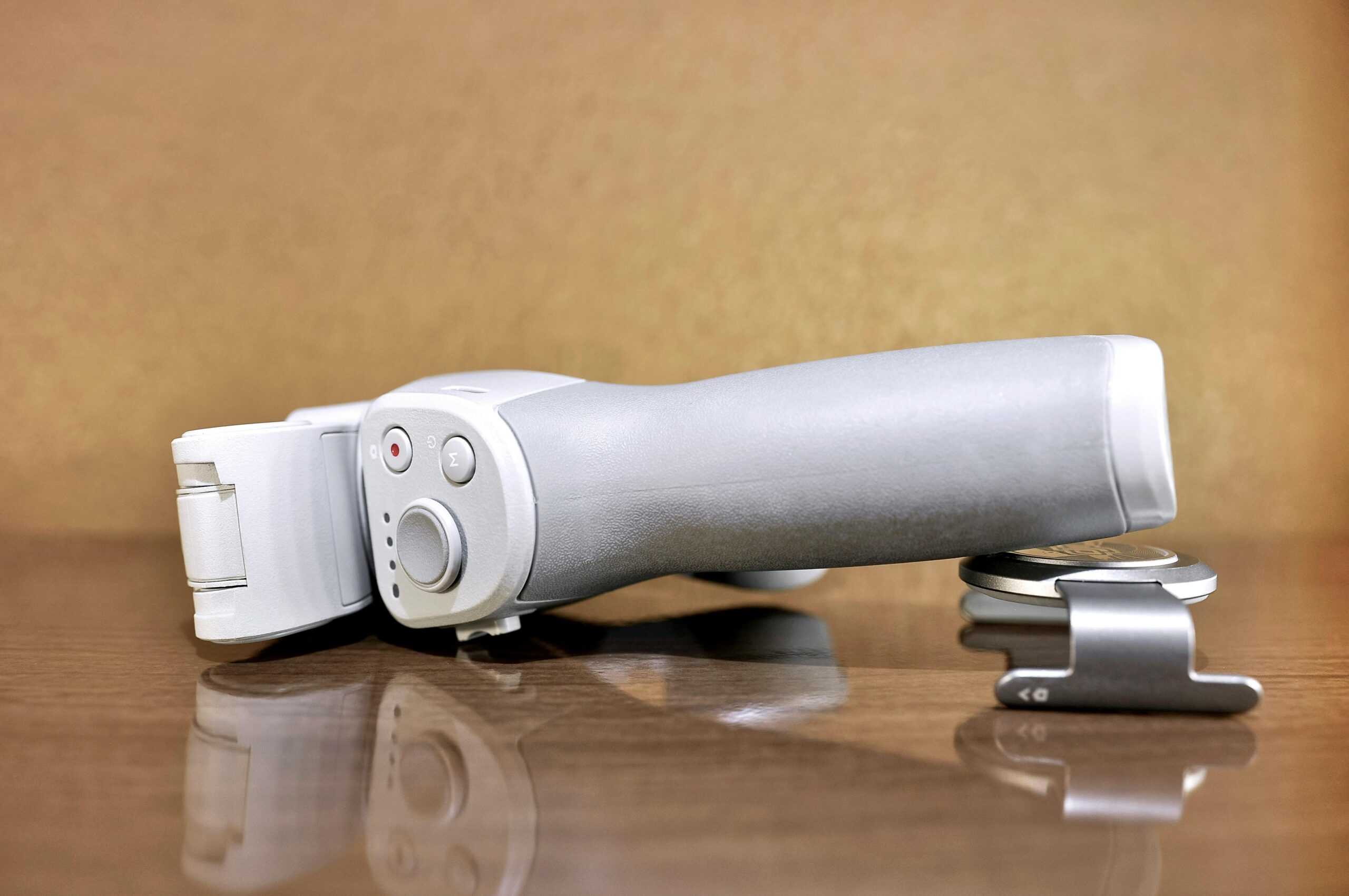 Detailed close-up of a handheld camera gimbal lying on a wooden surface, showcasing modern design and texture.